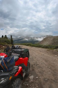 All-terrain-vehicle parked beside mountain trail with packs and helmets on cloudy day