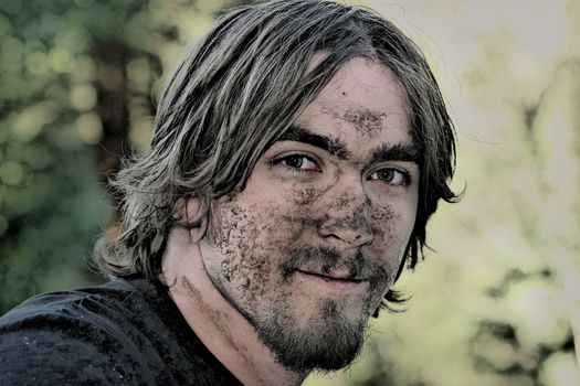 Handsome young man with his face covered with mud after negotiating a particularly muddy ATV trail.