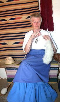 Mature woman spinning wool into yarn using drop spindle