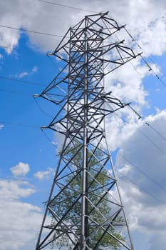 electric power pylon with tree growing inside it against cloudy blue sky