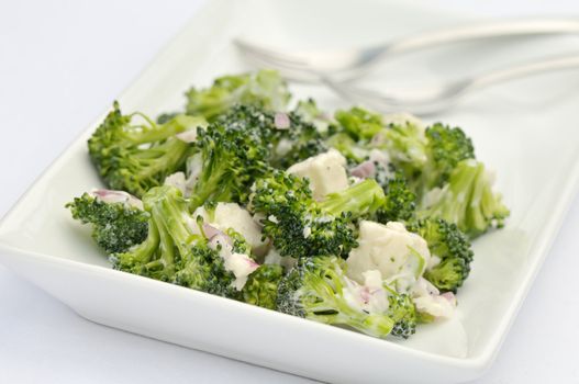 Broccoli and feta salad with shallots and caesar dressing on white platter