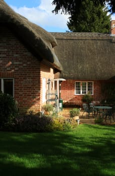 A ruraly located thatched cottage found in Wilthsire England. View of back of cottage showing thatched eves and garden patio area.