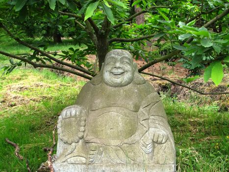 statue of a laughing Buddha under a tree