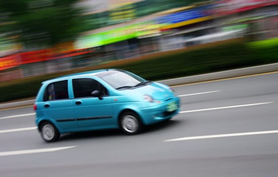 A light blue car speeding through a city centre. Motion blur was used for effect.