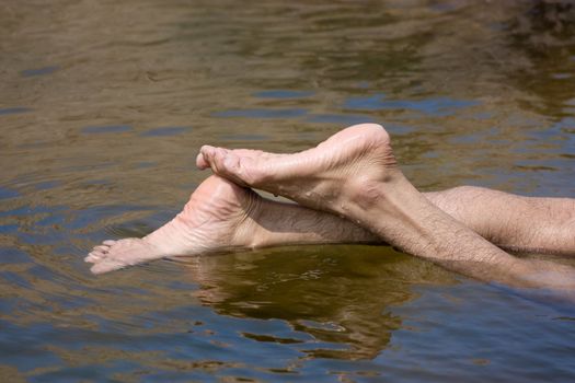 Feet of a man in the blue water of river 