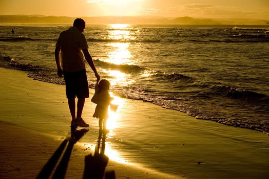 Young father walking with his little daughter along the beach at sunset, holding hands