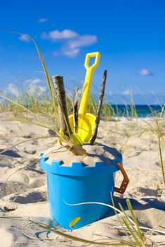 Child's toy bucket and spade in the sand on a beach, with sticks
