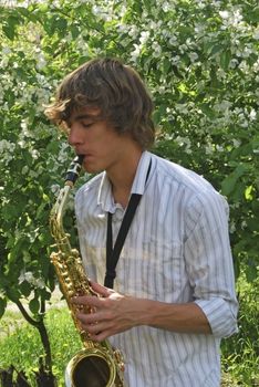 the young man with saxophone on the background of the flowering tree