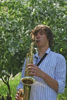 the young man with saxophone on the background of the flowering tree