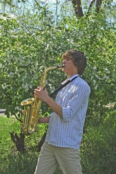 the young man with saxophone on the background of the flowering tree