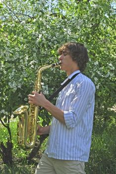 the young man with saxophone on the background of the flowering tree