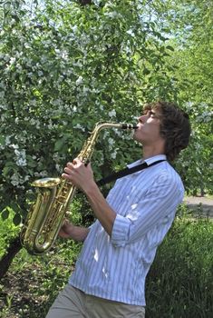 the young man with saxophone on the background of the flowering tree