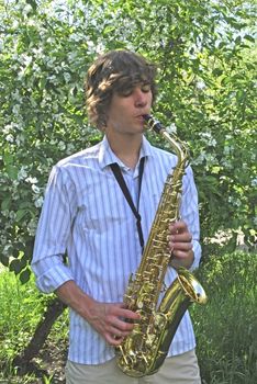 the young man with saxophone on the background of the flowering tree