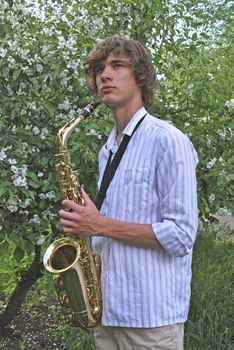 the young man with saxophone on the background of the flowering tree