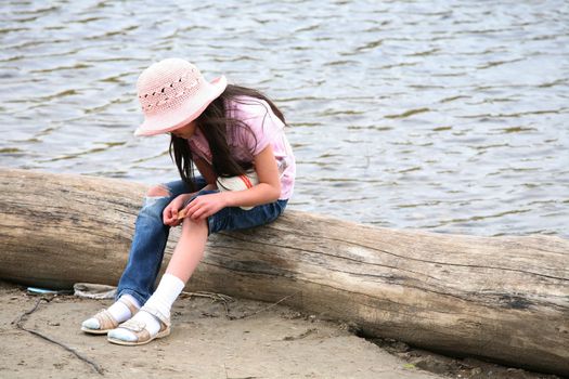 Girl with wound sitting on log by river