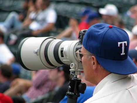A photographer taking pictures at a Texas Ranger baseball game.
