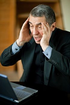 A businessman recoils from his laptop computer in horror.
