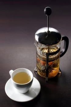 Transparent teapot with press by pervaded green tea near by white mug