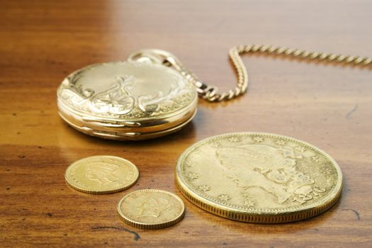 Gold watch and gold coins on wood surface