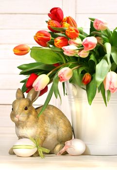 Little rabbit behind white container full of tulips