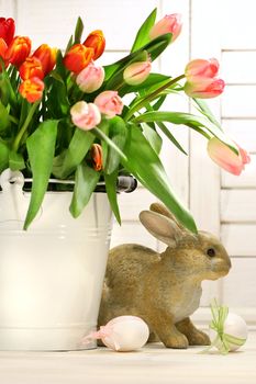 Rabbit hiding behind a white container of spring tulips