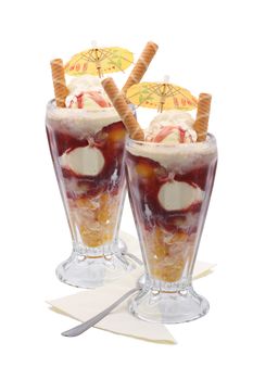 Two knickerbocker glory's filled with fresh fruit and ice cream topped with a paper umberalla decoration and some wafer's. Both in tall glasses with spoons and napkins.