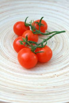 A platter of freshly picked organic cherry tomatoes on the vine, set on a wooden oval platter.