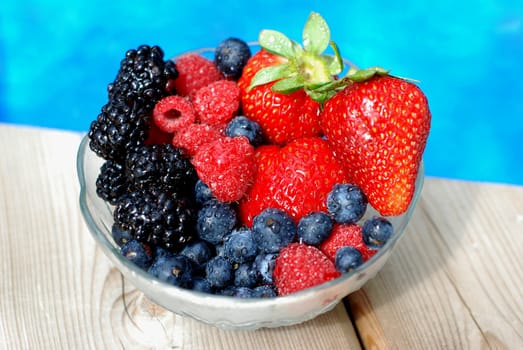 Bowl of mixed berries on a wooden deck near a pool