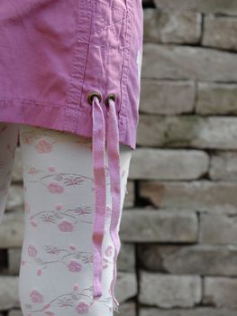 Fashion detail of female model wearing pink mini skirt and embroidered legwear with bricks in background