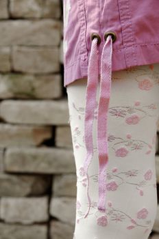 Fashion detail of female model wearing pink mini skirt and embroidered legwear with bricks in background - Slightly warm red toned