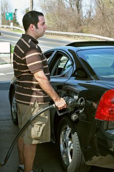 A man pumping high priced gas into his car with a disgusted look on his face.