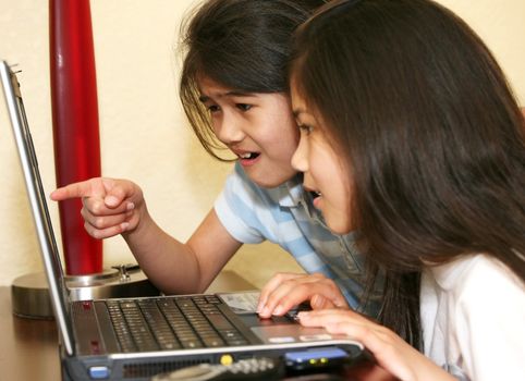 Two little girls working on a laptop  computer, pointing to screen in surprise
