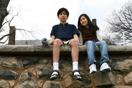 Two children sitting on rock ledge outdoors,  brother and sister