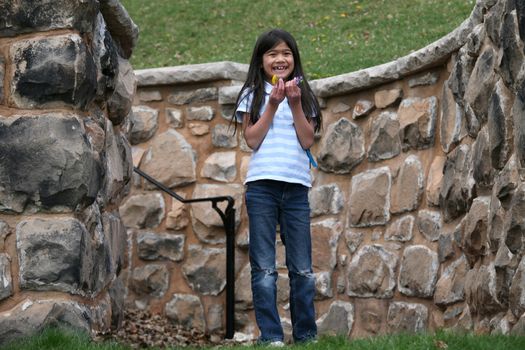 Happy little girl holding small flowers outdoors, standing between stone walls