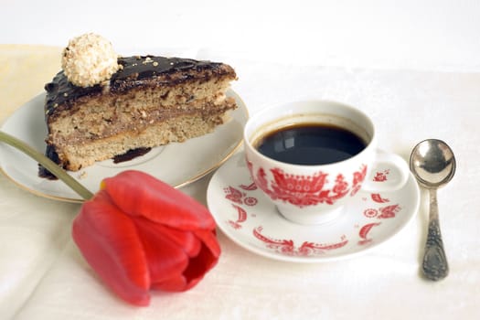 Piece of chocolate cake with coffee cup and red tulip on the table