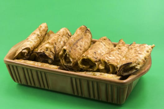 
	
Pancakes with meat in a ceramic dish on a green background