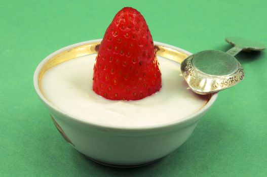 
Strawberries in the plates with yogurt and spoon on a green background 