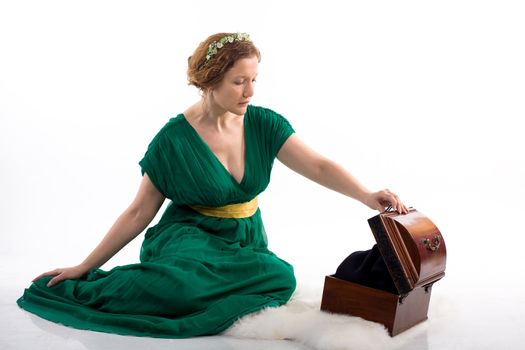 Lady in green antique dress opening box on white background
