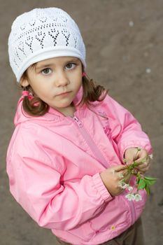 Portrait of thoughtful 3-year old little girl, holds blossoming cherry twig in her hands and looking at camera.