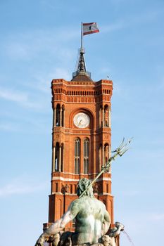 Tower of Rathaus the Berlin Town Hall made of red bricks with town flag and detail of the Neptune fountain.