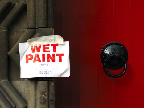 A 'wet paint' notice beside an old fashioned, freshly painted, bright red door.