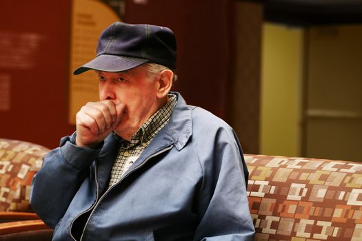 Senior man sitting in waiting room of hospital coughing