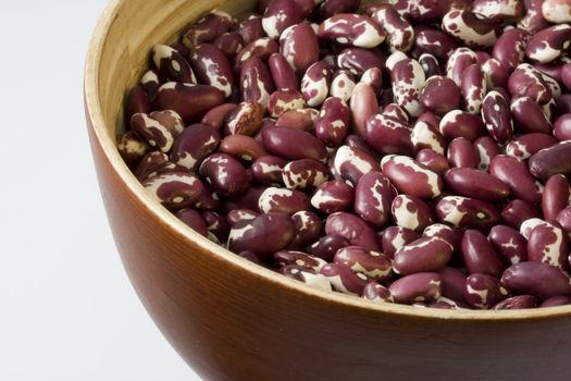 a wooden, round bowl of purple and white anasazi beans, white background, copy space
