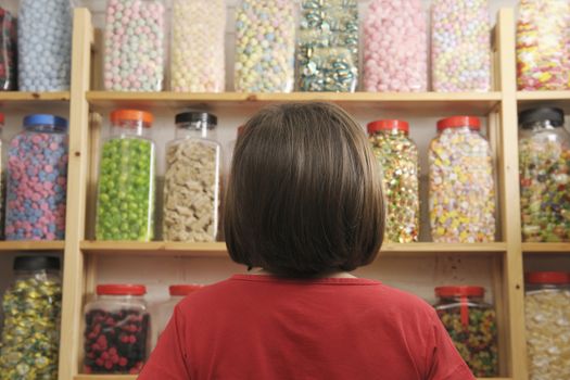young girl looking at rows of sweets in shop