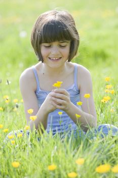 young female child sitting cross legged in a field full of buttercups smiling