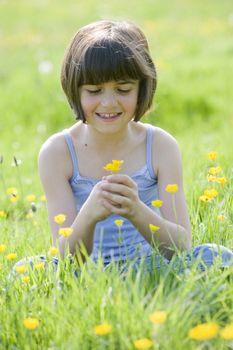 young female child holding buttercups while sitting in field and smiling