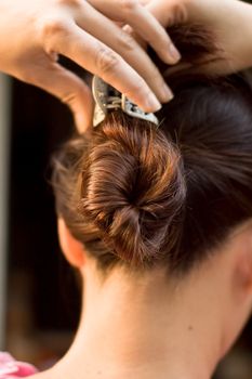 A woman twirling her hair and tying it with hair clip with both hands. view from behind