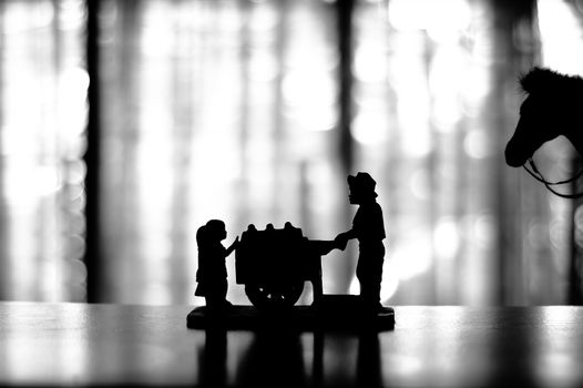 Silhouette of a figurine of an ice cream cart vendor selling to two kids with a horse on the background