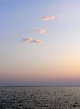 Landscape at sunset with reflection in sea water and few pink clouds in sky.