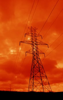 The silhouette of a power lines and towers against an ominous orange sky.
